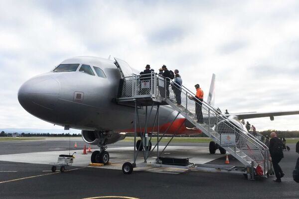 A plane sits on the tarmac at Hobart Airport as people walk up the stairs to board it.