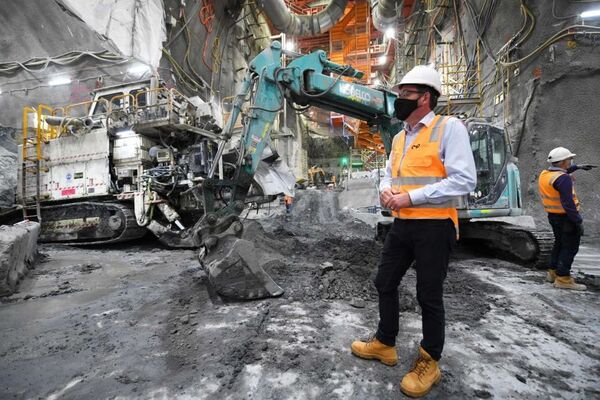 Daniel Andrews, dressed in a hard hat and high-vis, stands in front of heavy machinery on a construction site.