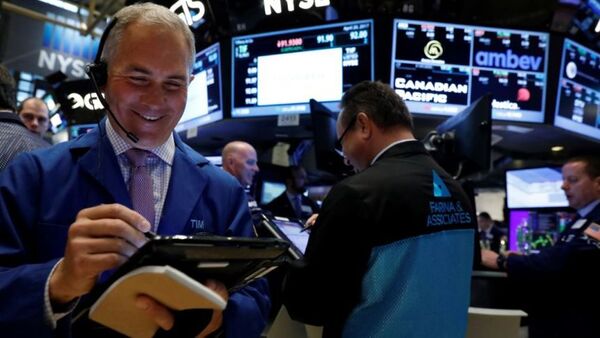 Traders work on the floor of the New York Stock Exchange, with one man seen in the front left writing on a screen and smiling. A headset sits atop his head.