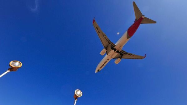 The white, red and silver underside of a Qantas plane is seen flying over a clear blue sky in Adelaide.