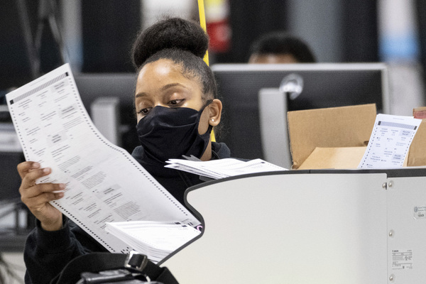 worker in a mask scans ballots as the presidential recount process gets under way in Georgia