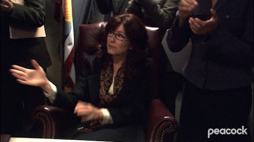 The character of Laura Roslin from the television show Battlestar Galactica applauds while her team does the same around her.