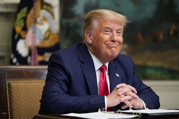 Donald Trump smiles while sitting at a desk.
