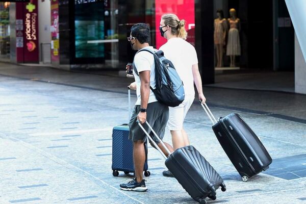 People carrying luggage wear face masks as they make their way through the CBDB of Brisbane.