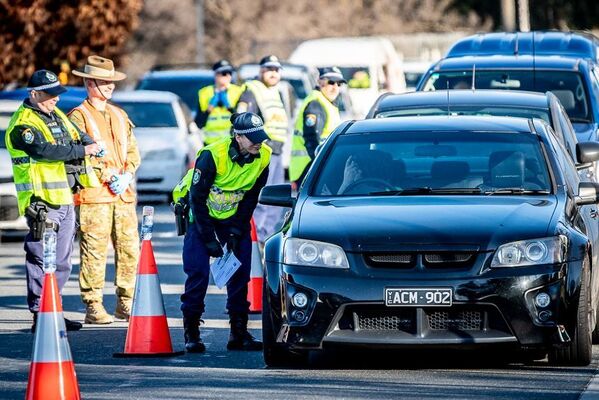 A handful of police stand in front of a line of cars queueing at a border.