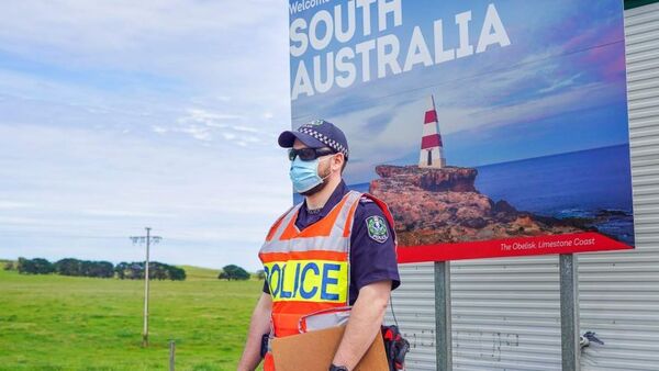 a masked police officer stands in front of the 'welcome to south australia' sign