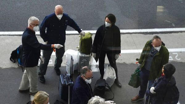 a group of masked travellers stand outside a hotel with their bags.