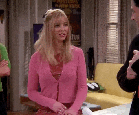 Phoebe from Friends says Good luck good luck good luck! We all wish you good luck in a GIF. She stands in a living room wearing a pink cardigan and raises her hands above her head.