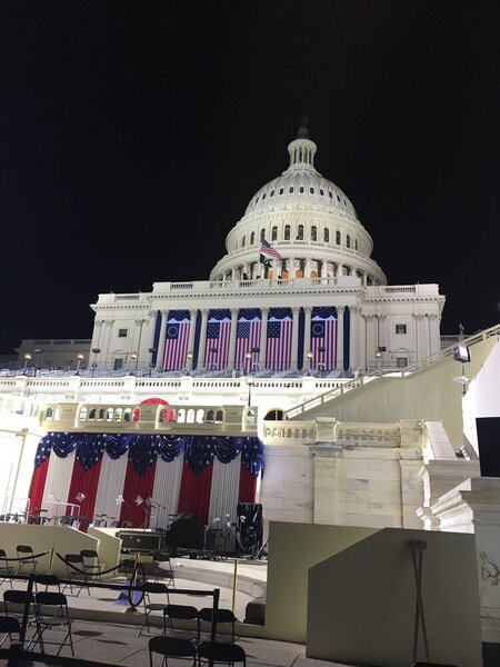 The US Capitol building is seen draped in flags with a stage in front. The sky above is black.