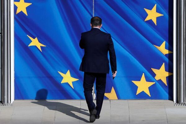 A man in a suit walks toward double doors emblazoned with the EU flag. 