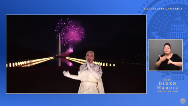Katy Perry, in a white gown and gloves, stands in front of a fireworks display on the National Mall in Washington DC