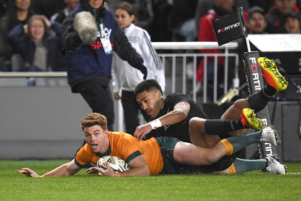 A Wallabies winger holds the ball with his left hand as he scores a try against the All Blacks.