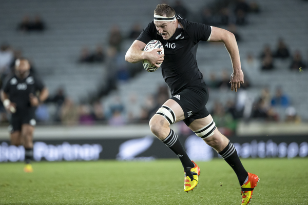 An All Blacks lock holds the ball with his right hand as he runs against the Wallabies.