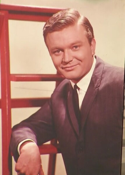 A young Bert Newton casually poses propped on his elbow, dressed in a suit.