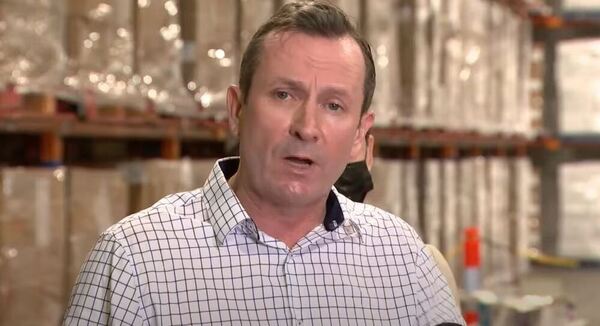 WA Premier Mark McGowan standing in a warehouse with shelves stocked with boxes.
