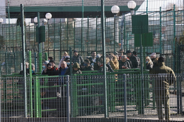Behind lines of fencing, people queue