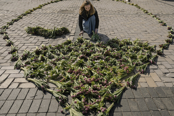 A woman adds bundles of tulips to a pattern lying on cobbles.