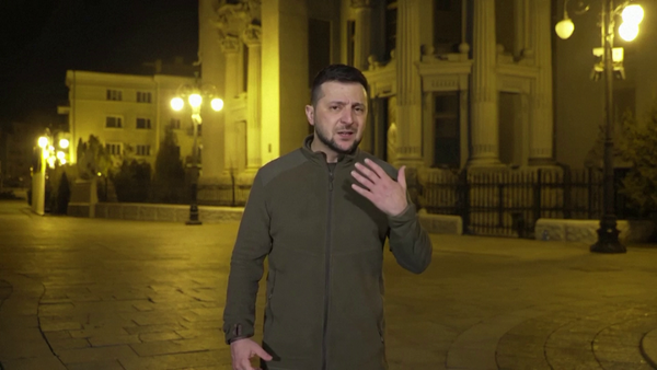 Volodymyr Zelenskyy stands in front of a lit building at night.