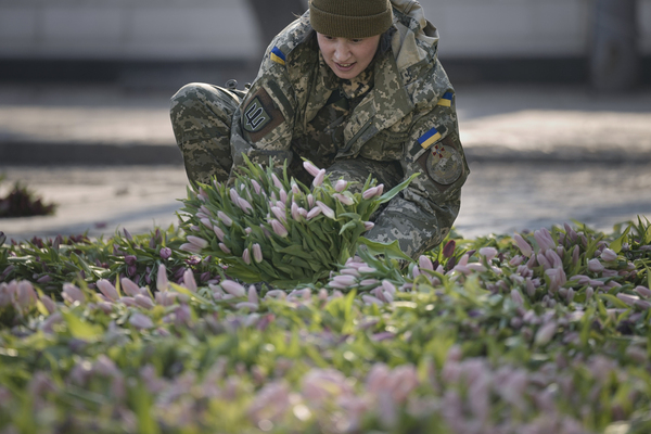 A Ukrainian servicewoman lays tulips on the ground.