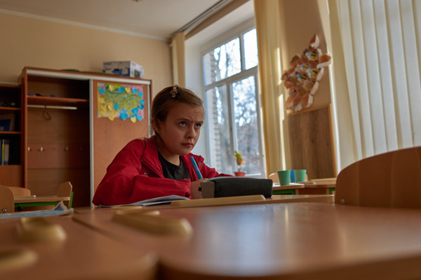 A little girl frowns while concentrating on her school work, holding a pen at a desk