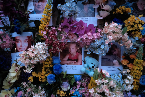 A close up of the wall - pictures of young children, women and men are pinned on the wall next to flowers and teddy bears