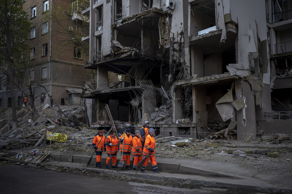 A group of people dressed in bright orange walk by a building in ruins