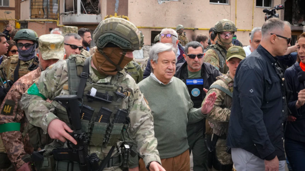 Mr Guterres, wearing a green jumper, walks surrounded by armed soldiers