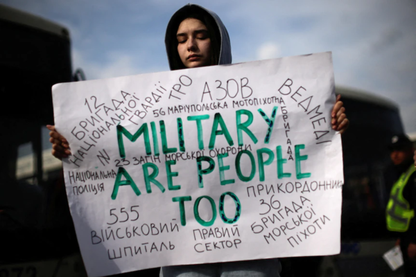 a woman with her eyes shut holds up a hand painted sign that reads Military are people too