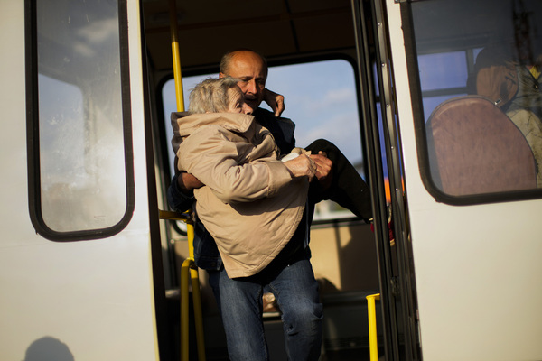 A man carries an old woman off a bus