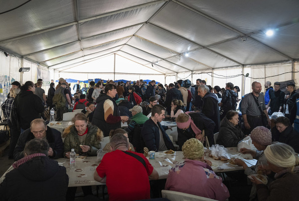 hundreds of people mill around a large tent where tables are laden with food