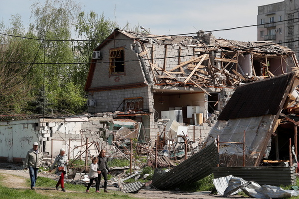 a family walks past a house half collapsed