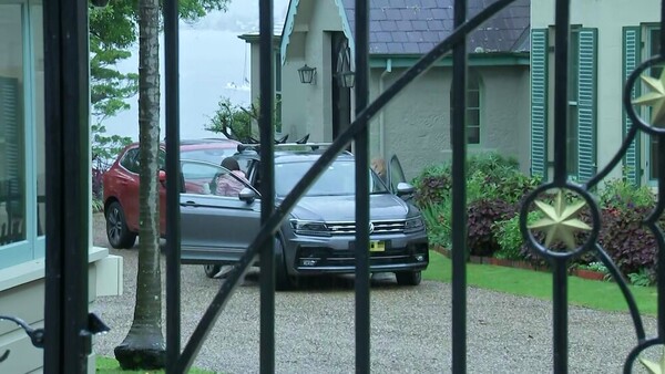 Through a gated fence, a women gets out of a car in the driveway.
